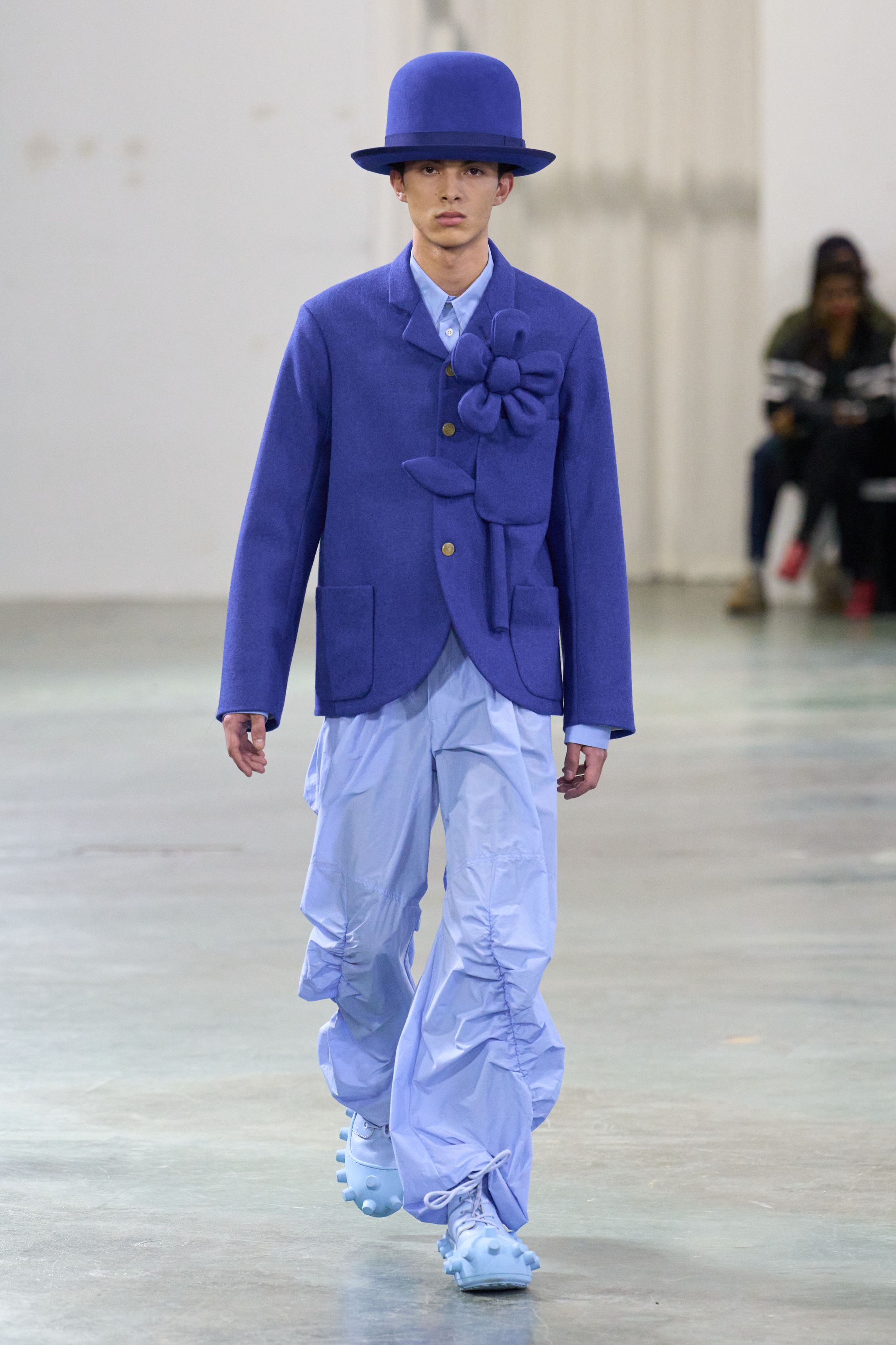 Walter Van Beirendonck 2026秋冬以高度饱和的色彩、夸张比例与童真符号继续挑战男性气质的既定边界。针织花朵、卡通图案、结构化西装与机能裤装并置，构建出介于游戏、政治隐喻与乌托邦幻想之间的舞台。系列拒绝低调，刻意制造视觉噪音，用快乐、怪诞与不合时宜的色彩作为对现实焦虑的反击，呈现一场毫不妥协的时装宣言-顽石频道趋势研究